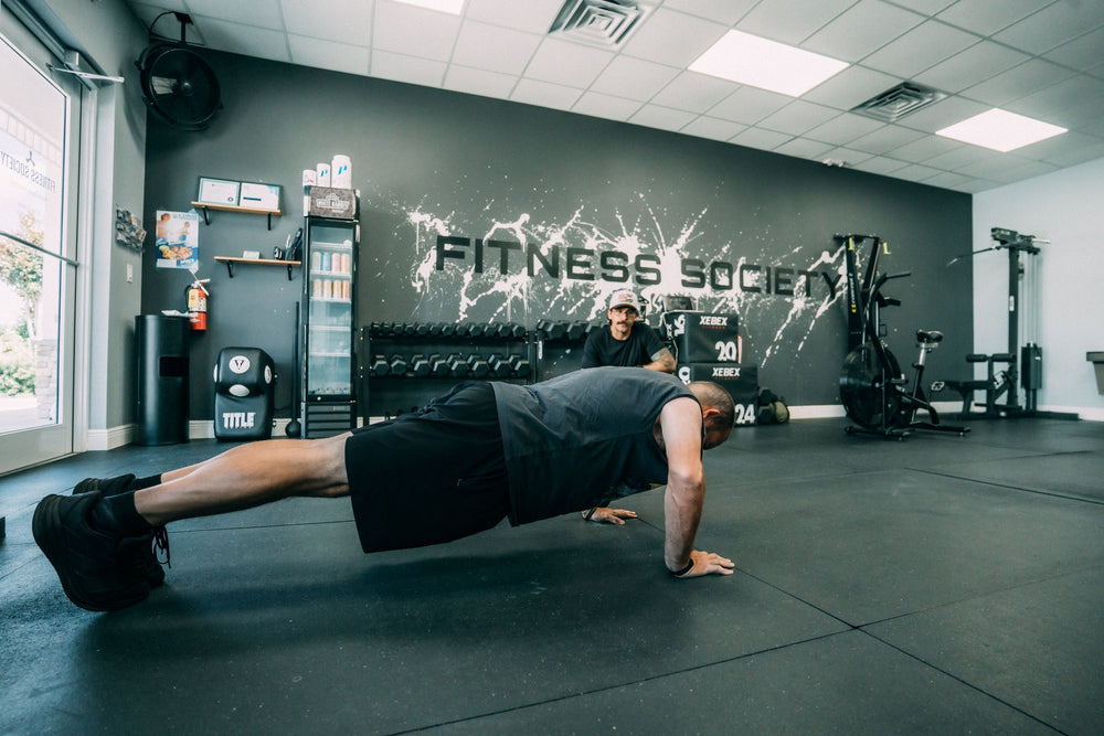 Client holding a plank under the Fitness Society logo wall