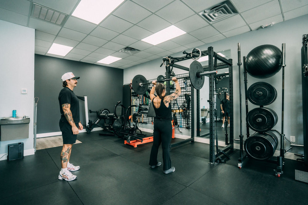 Woman pressing a barbell overhead with her personal trainer