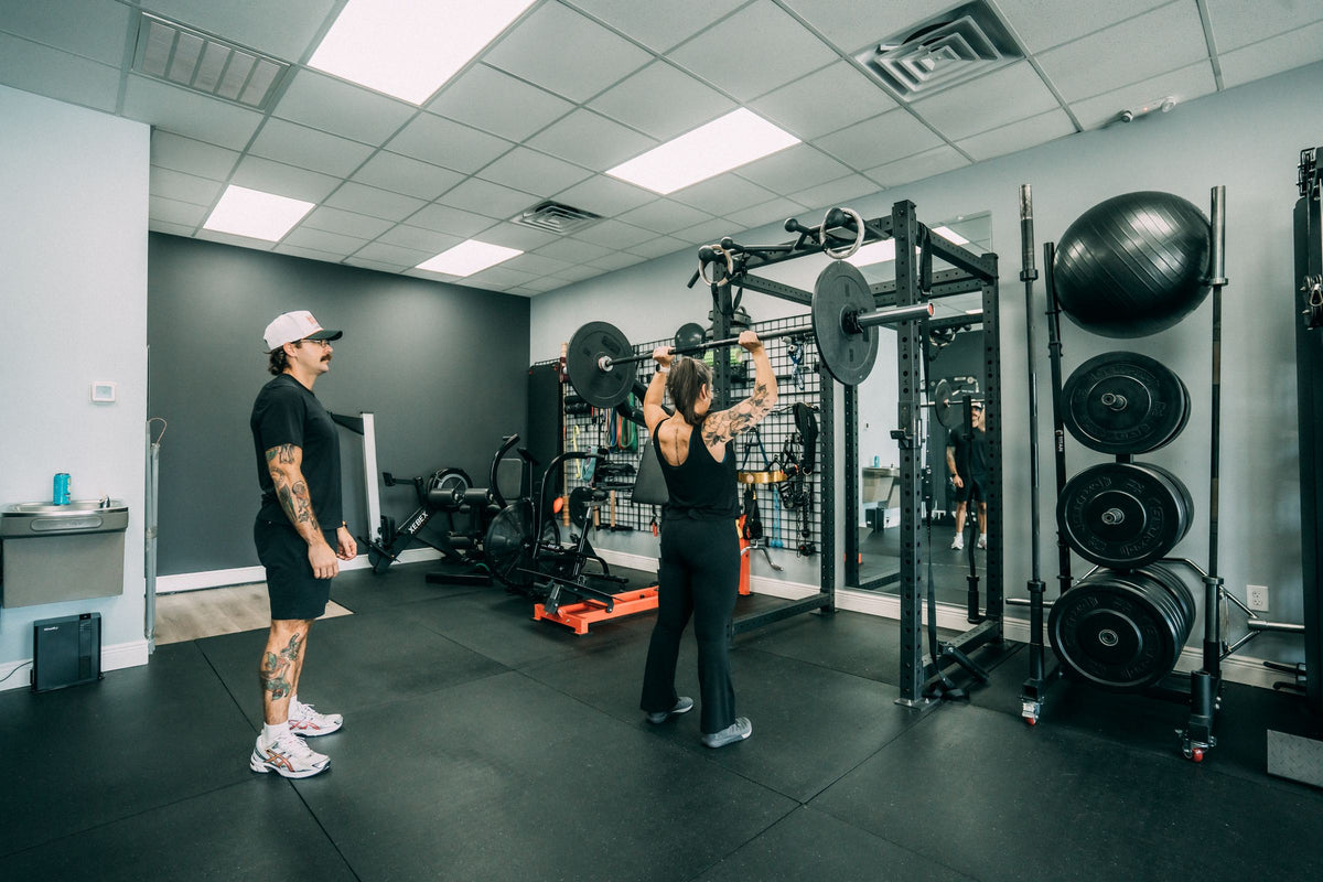 Woman pressing a barbell overhead with her personal trainer